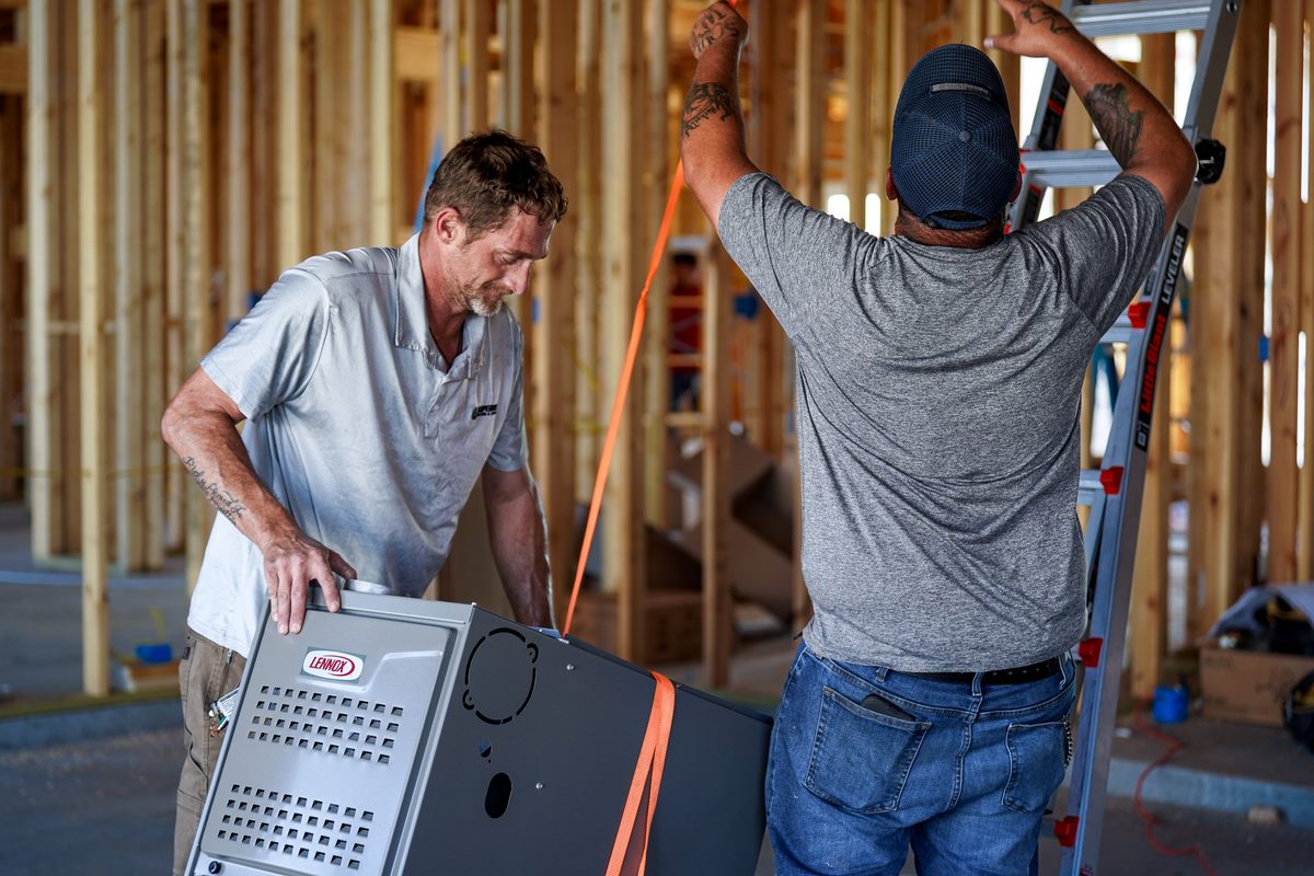 Two Superior Heating & Cooling installers setting a new furnace into place on a job site