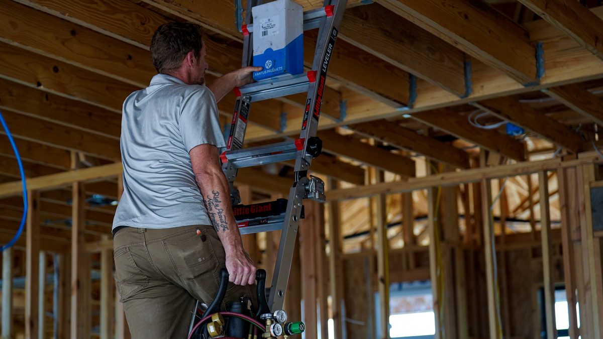 Superior Heating & Cooling installer on a ladder fitting equipment in a house still being framed