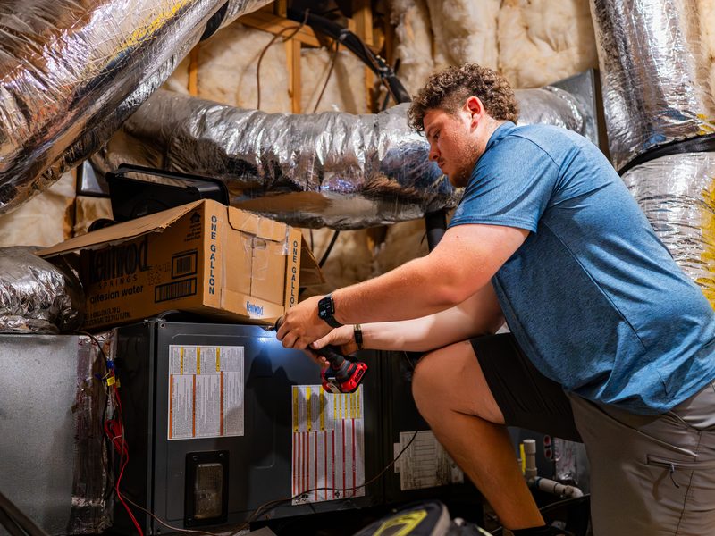 Technician inspecting an air handler blower by flashlight during a repair call