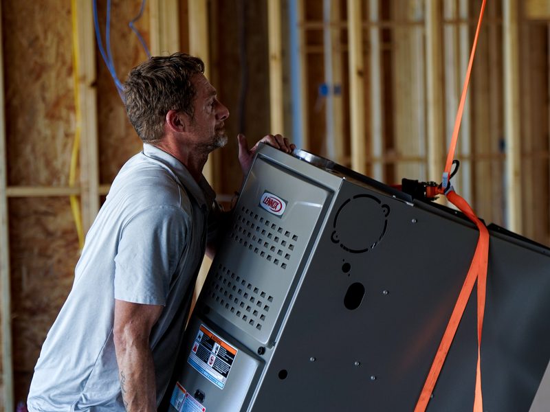Installer carrying a new furnace into place for a system replacement
