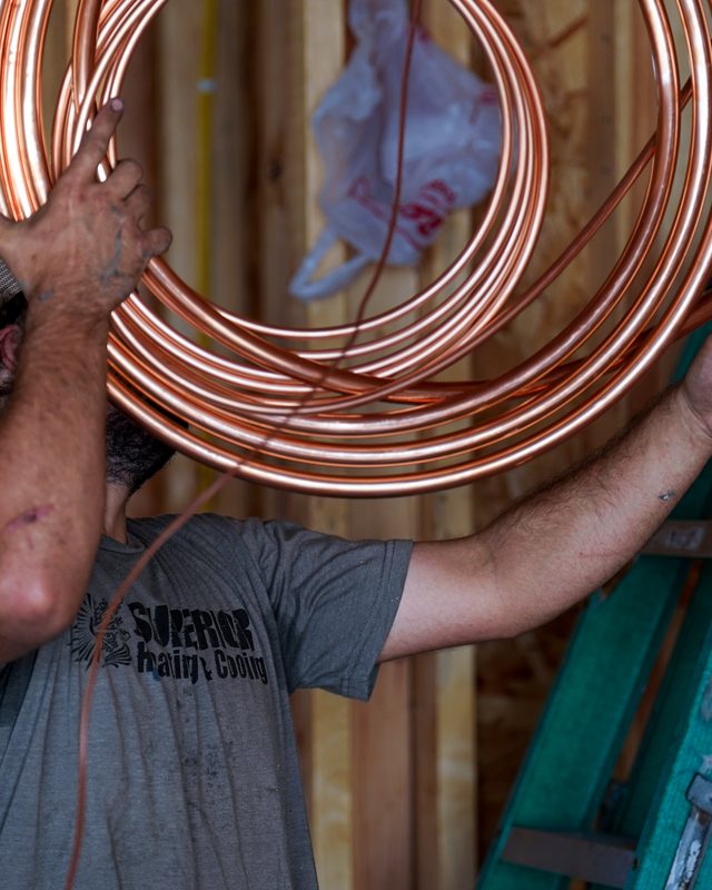 Installer lifting a coil of copper line set into a house under construction